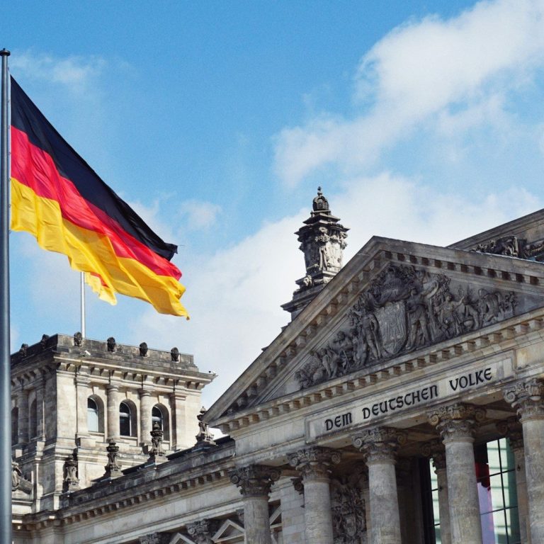 Finanzminister Bundesflagge vor dem Reichstagsgebäude in Berlin unter blauem Himmel.